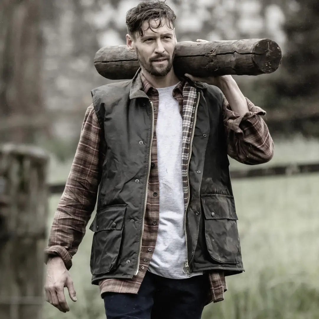 Man in outdoor work clothes with log, rocking a Fife Padded Waxed Waistcoat