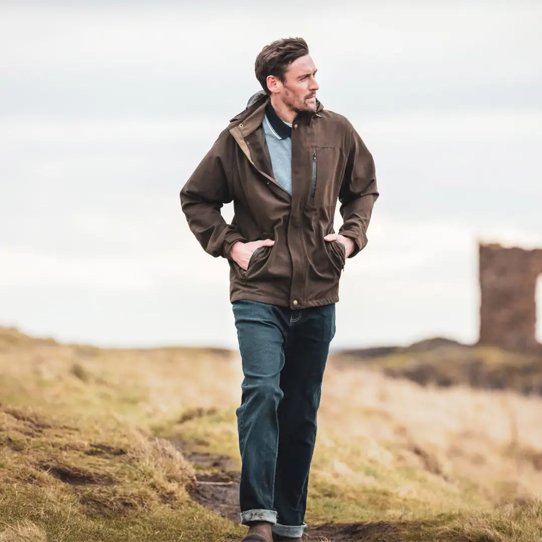 Man in a brown jacket exploring grassy terrain in a Fife Struther Waterproof Jacket