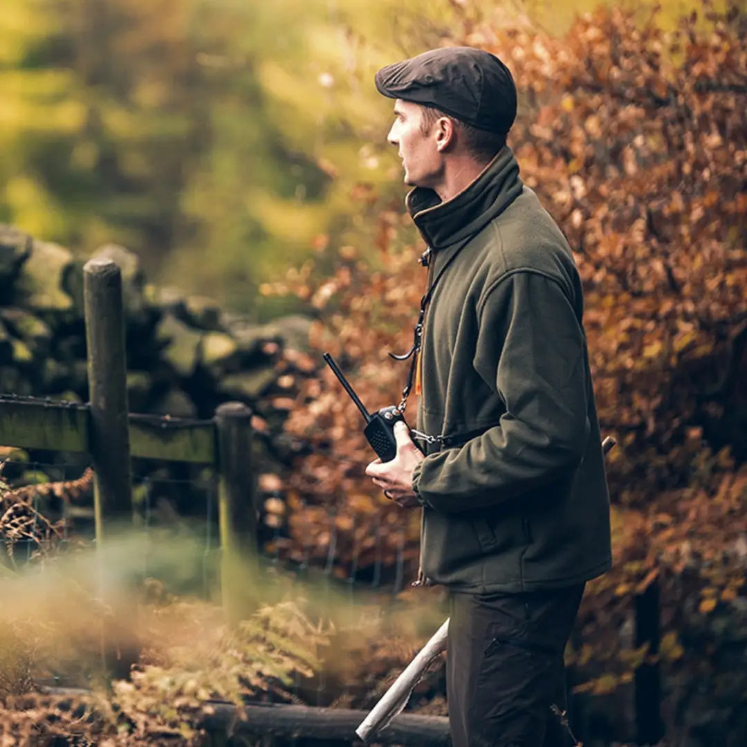 Man in a Jack Pyke Ashcombe Flat Cap and green jacket holding a camera in autumn