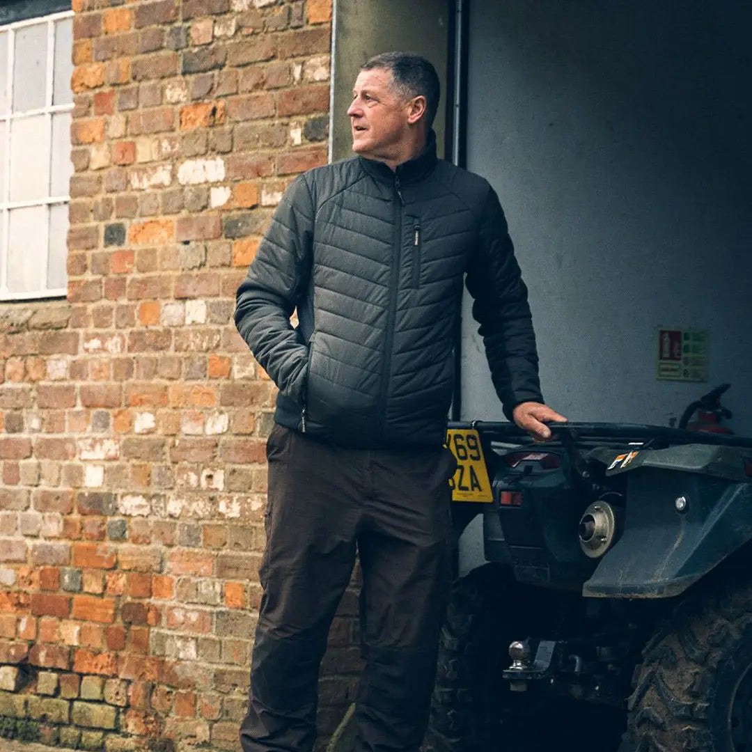 Man in a dark Jack Pyke Hybrid Quilted Jacket leaning against a brick wall