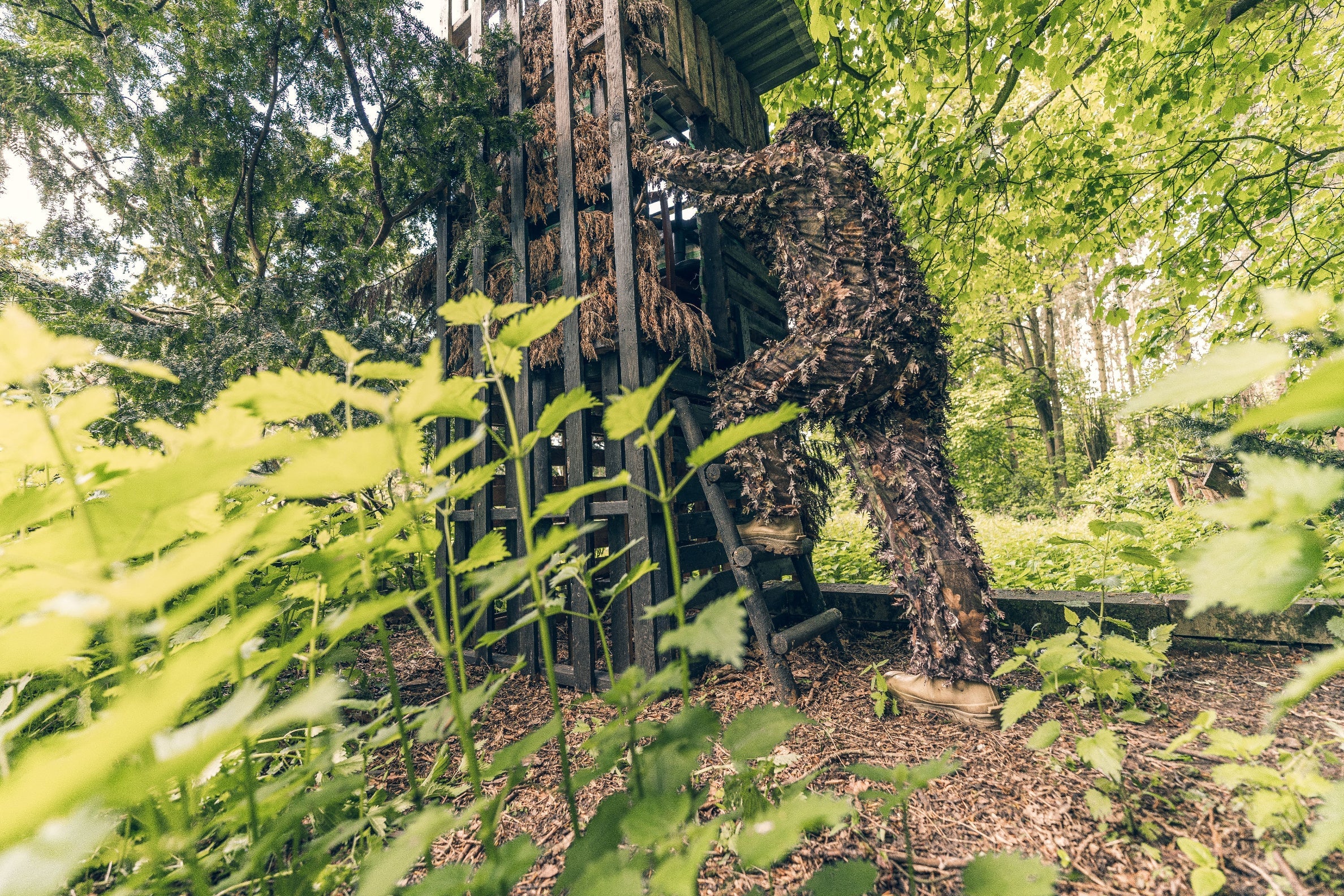 Camouflaged figure scaling a wooden tower in Jack Pyke LLCS 3D Concealment Suit