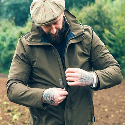 Person zipping up an Olive Green Jack Pyke Pro-Lite Hunters Jacket with a flat cap