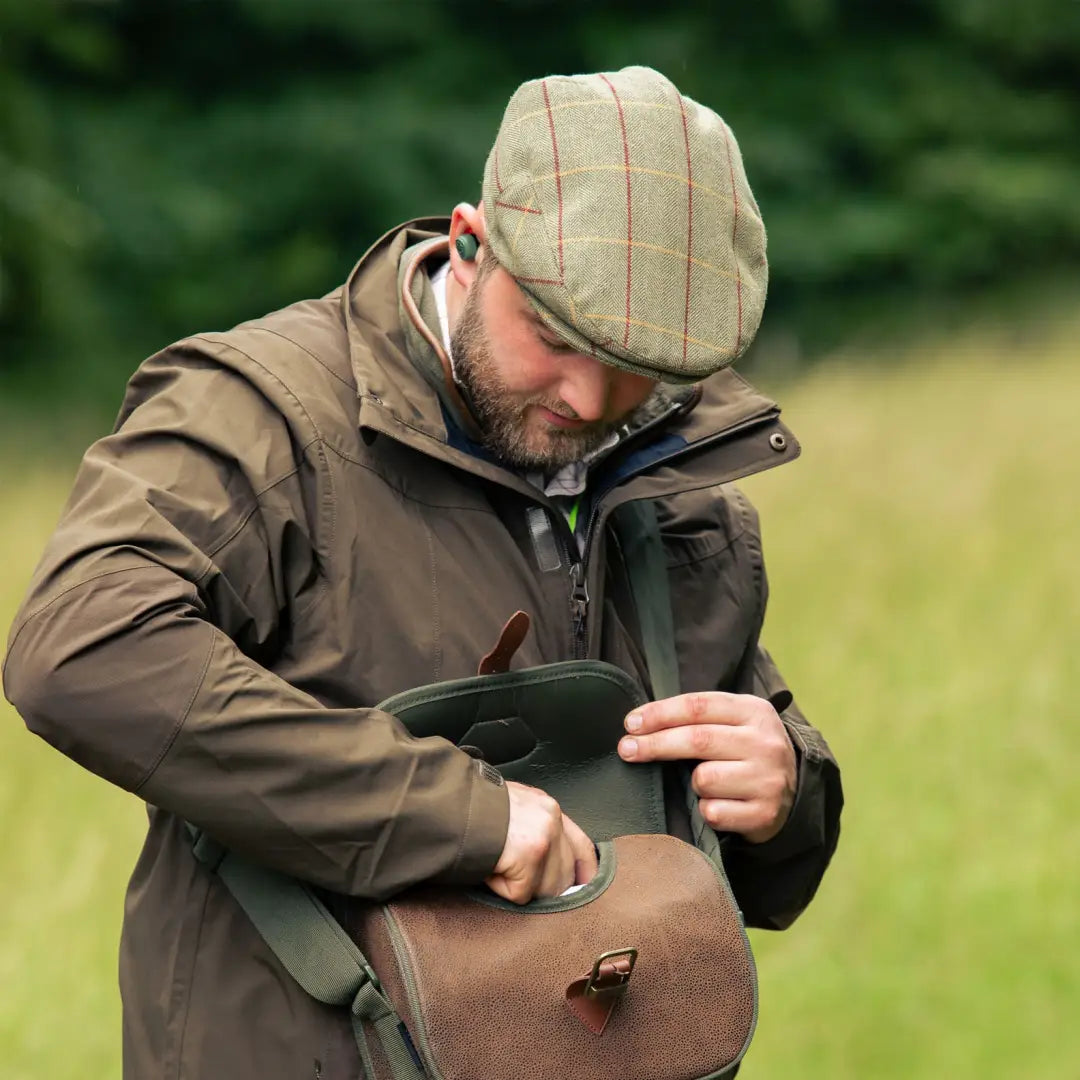 Bearded man in a flat cap and jacket checking his bag featuring Jack Pyke wool blend