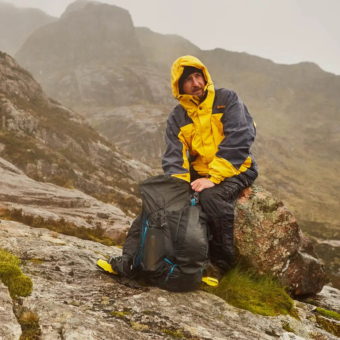 Hiker in a bright yellow and gray Keela Munro Jacket sitting on a rock with a backpack