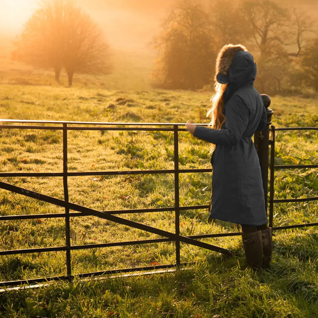 Person in a coat leaning on a metal gate at sunset in a stylish Crofter Parka