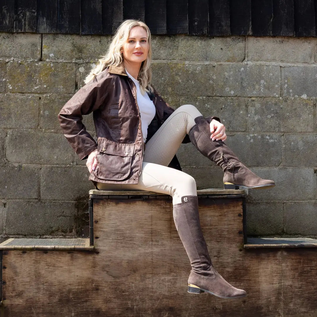 Woman in brown leather and knee-high boots with an Antique Wax Jacket seated on wood