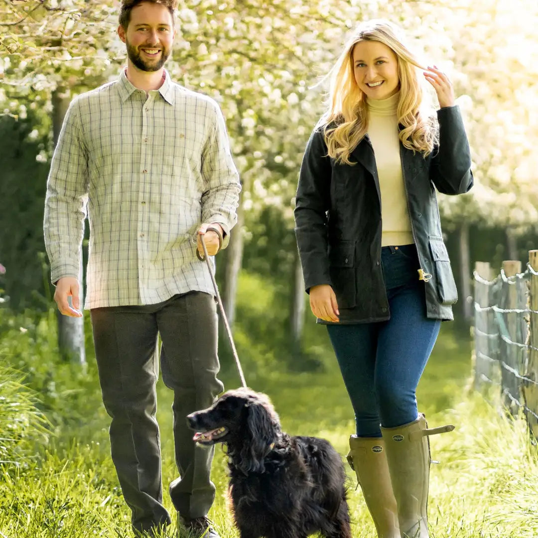 Couple walking a black dog on grassy path in stylish Ladies Antique Wax Jacket