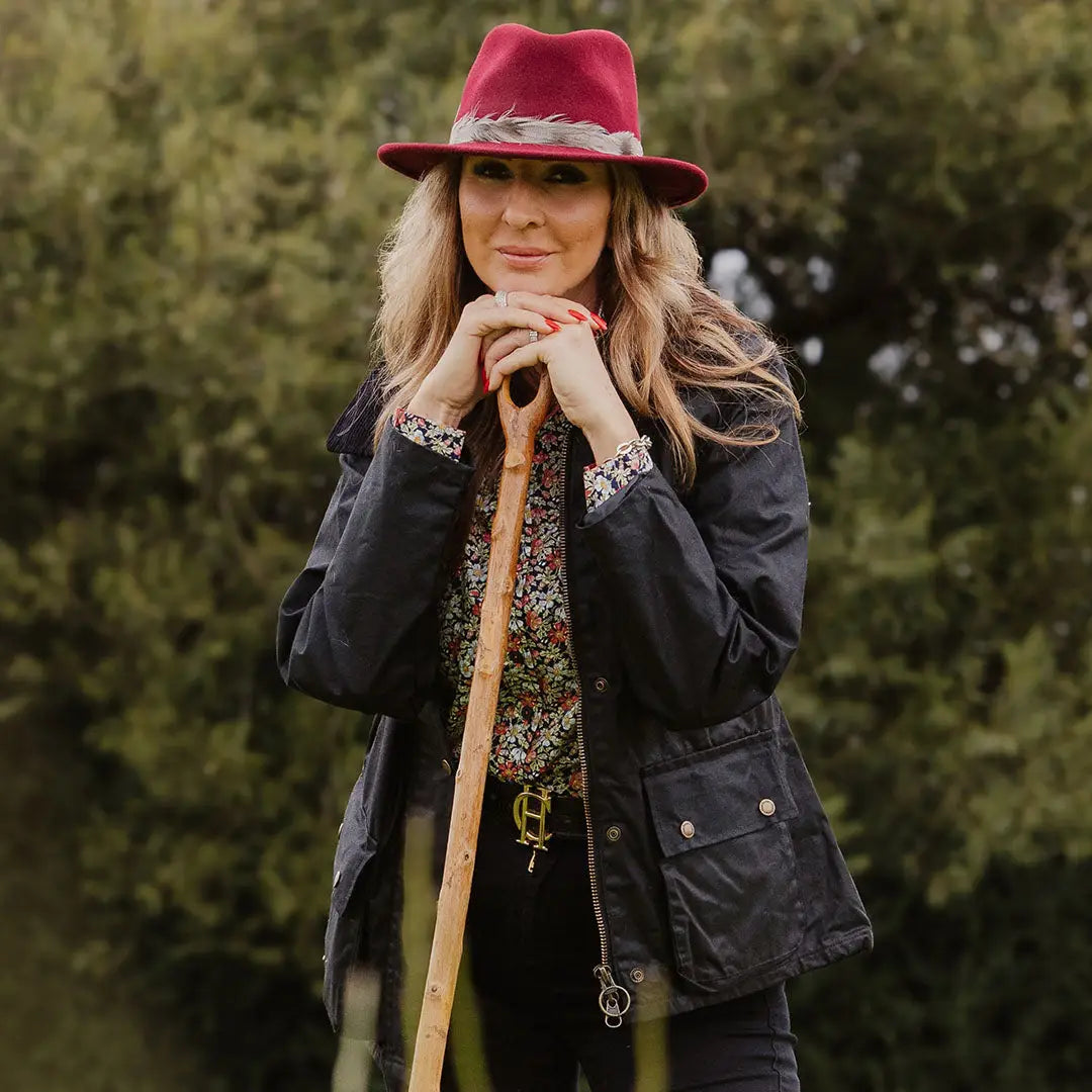 Woman in a red hat and black jacket with a wooden staff showcasing Ladies Antique Wax Jacket