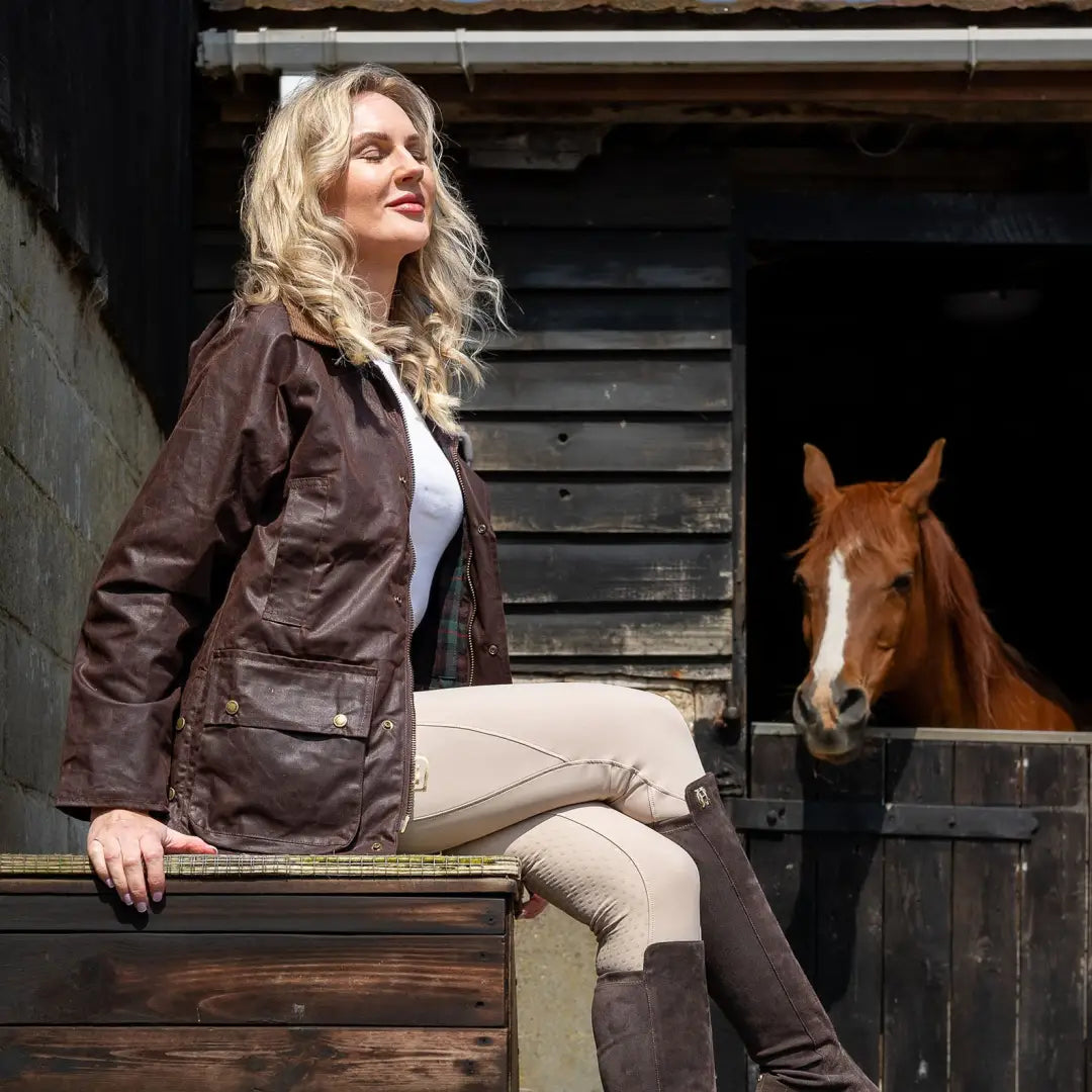 Woman in a brown Antique Wax Jacket sitting near a horse stable, showing style and comfort