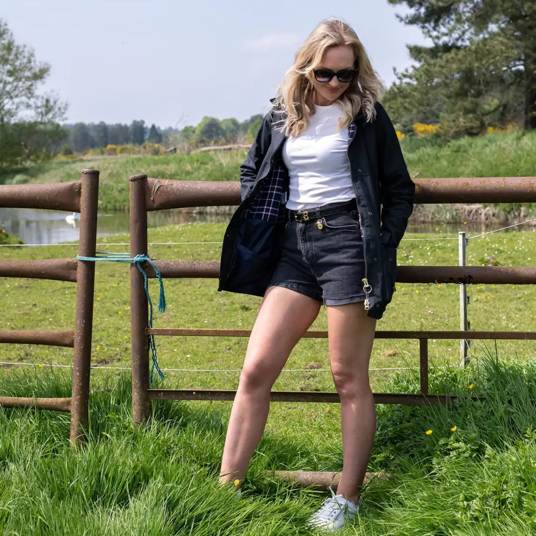 Woman in casual outdoor attire showing off a Ladies Traditional Wax Jacket by a fence