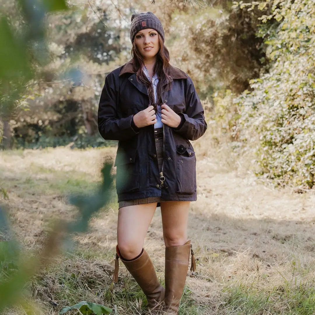 Woman in a dark traditional wax jacket and purple beanie standing outdoors