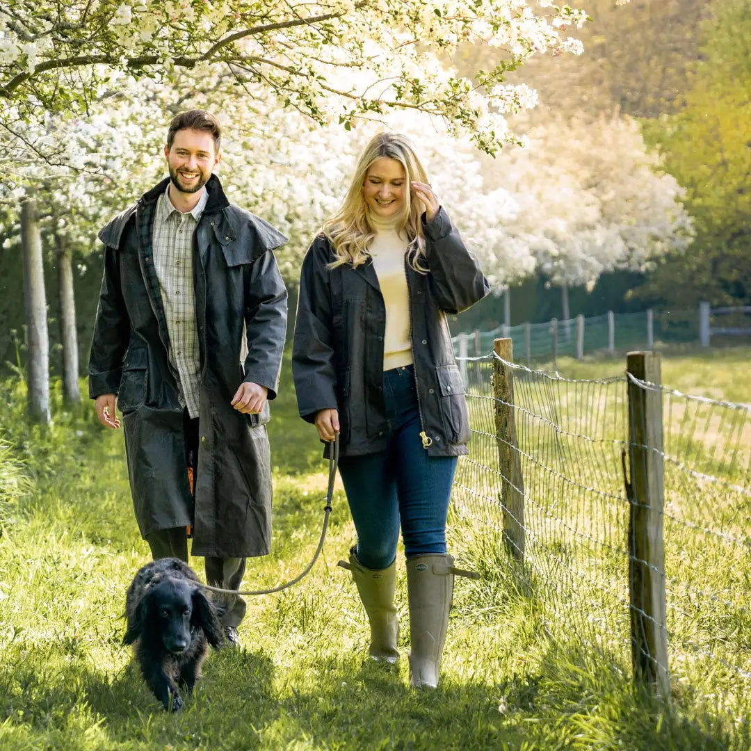 Couple in a traditional wax jacket walking a dog under cherry blossoms