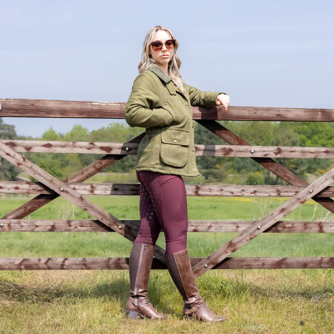 Woman in a green tweed jacket with purple pants by a wooden fence