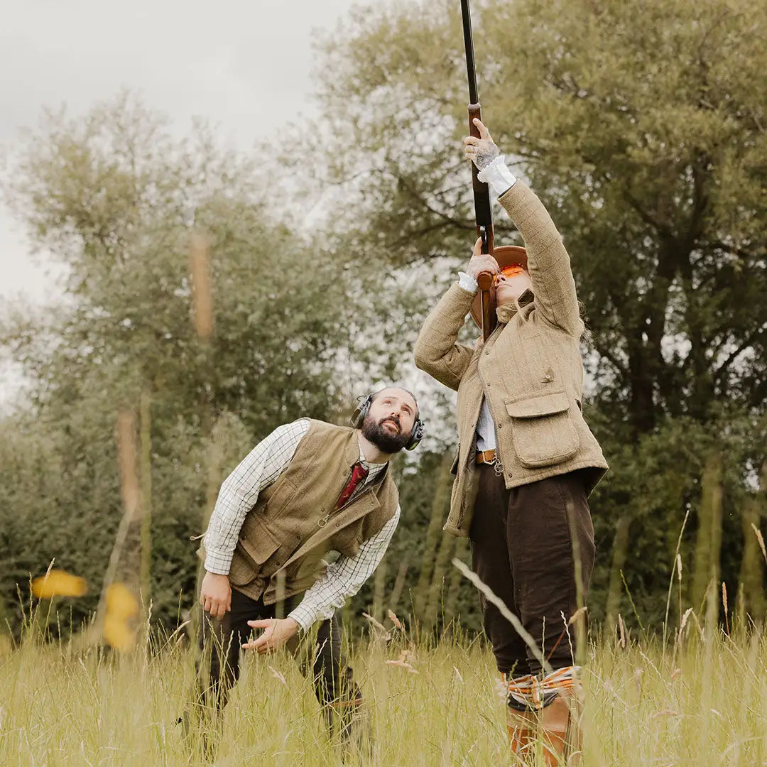 Two men in hunting attire aiming shotguns in a grassy field, showcasing ladies tweed jacket