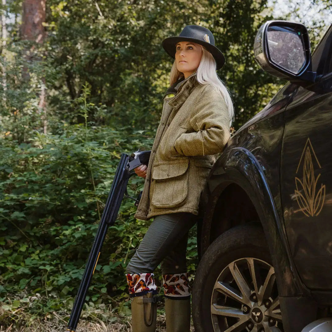 Woman in a fantastic quality ladies tweed jacket with shotgun by a vehicle