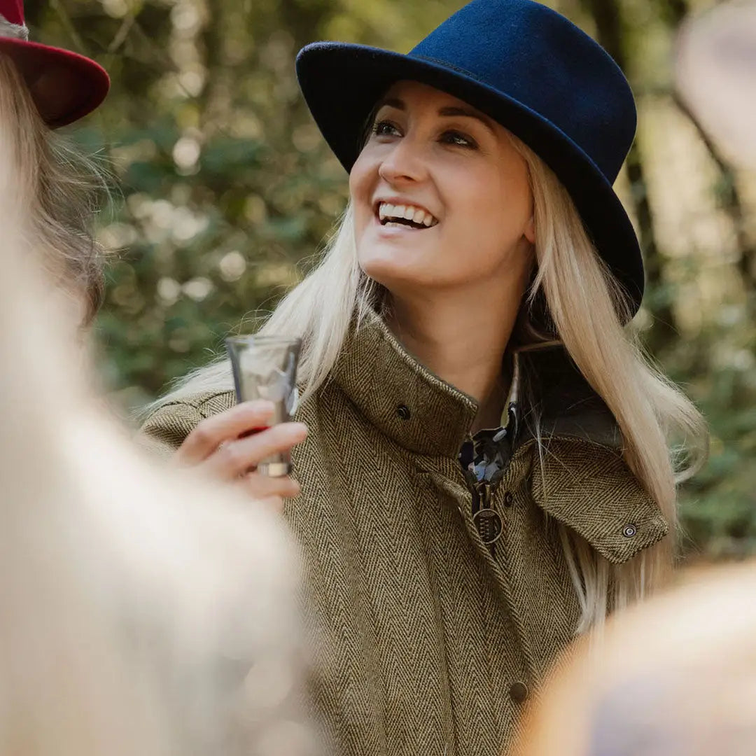 Smiling blonde woman in blue hat and olive green coat showcasing ladies tweed jacket