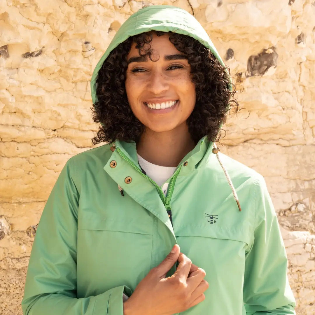 Smiling person in a mint green Lighthouse Beachcomber Coat, a stylish lightweight waterproof jacket