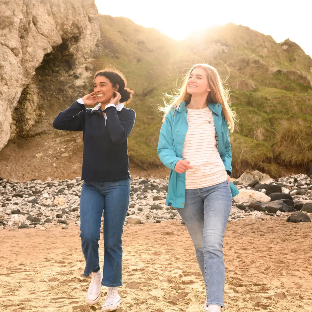 Two women in Lighthouse Beachcomber Ladies Waterproof Jackets walking by rocky cliffs