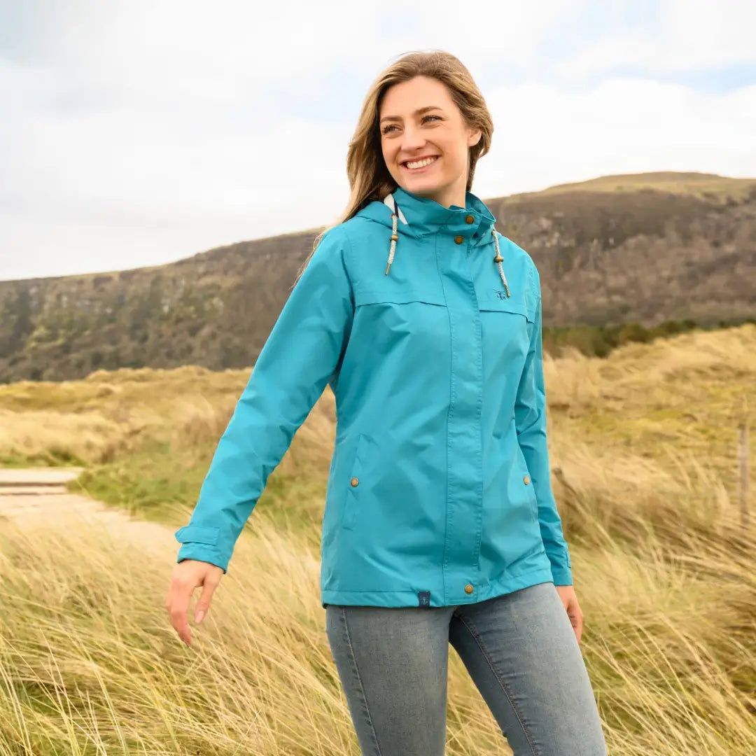 Smiling person wearing a bright turquoise Lighthouse Beachcomber Ladies waterproof jacket