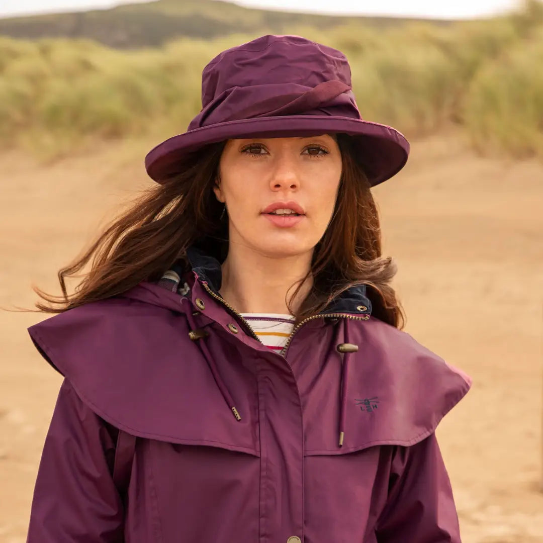 Woman in a purple rain hat and jacket wearing the Lighthouse Canterbury Waterproof Ladies Hat