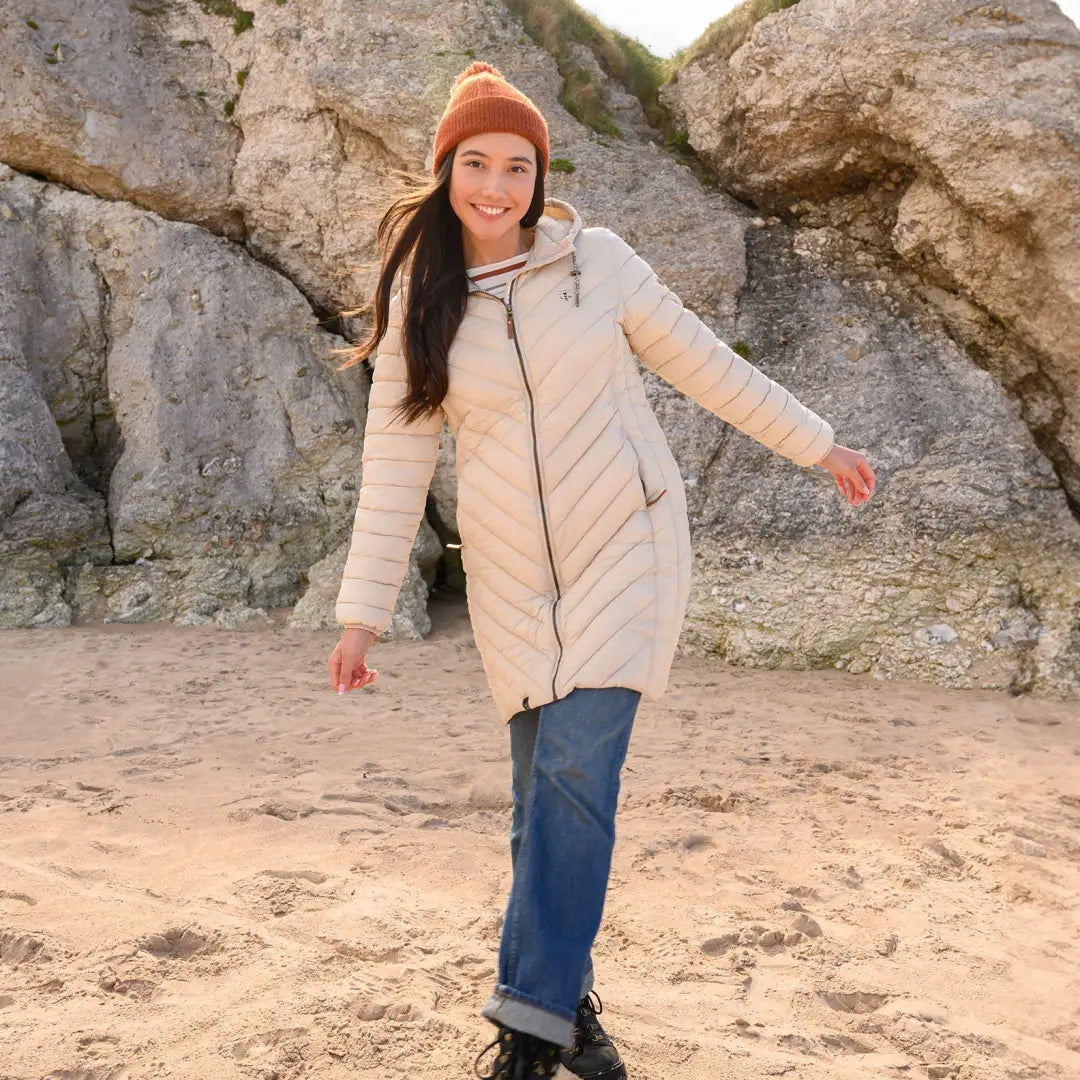 Woman in a beige mid-length coat enjoying the beach near cliffs, showcasing coat offers