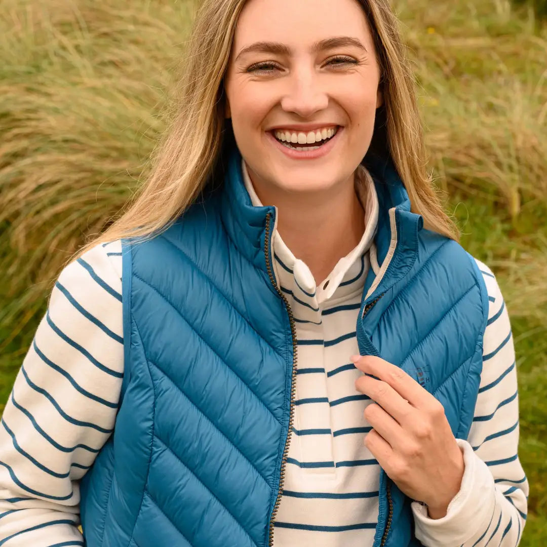 Smiling woman in a blue puffer Laurel Gilet over a striped shirt, cozy and stylish