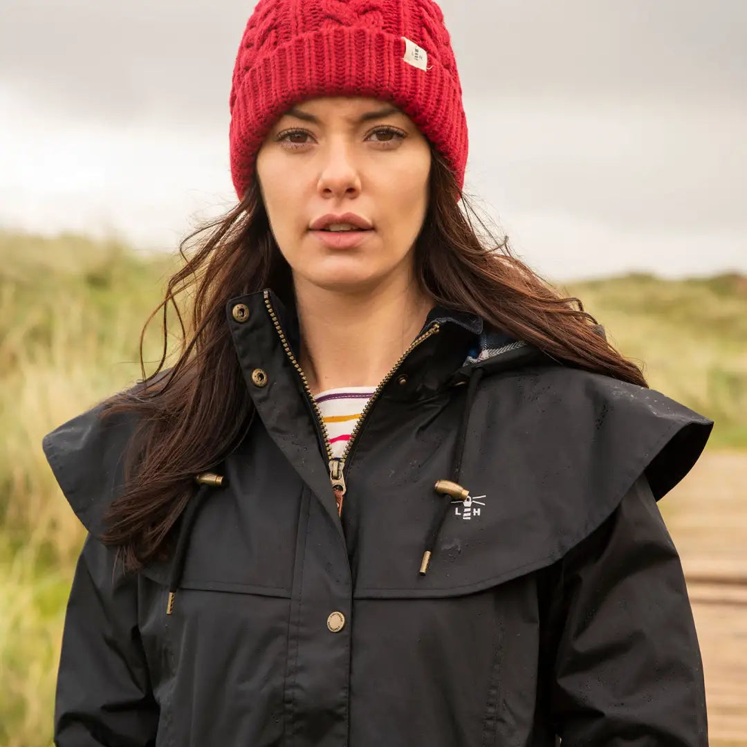 Woman in a red knit hat and black jacket wearing Lighthouse Outback length ladies waterproof raincoat outdoors