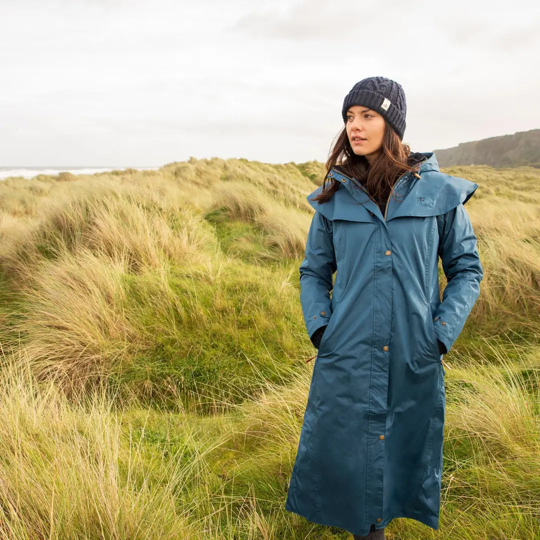 Long teal Lighthouse Outback waterproof raincoat in a grassy coastal setting