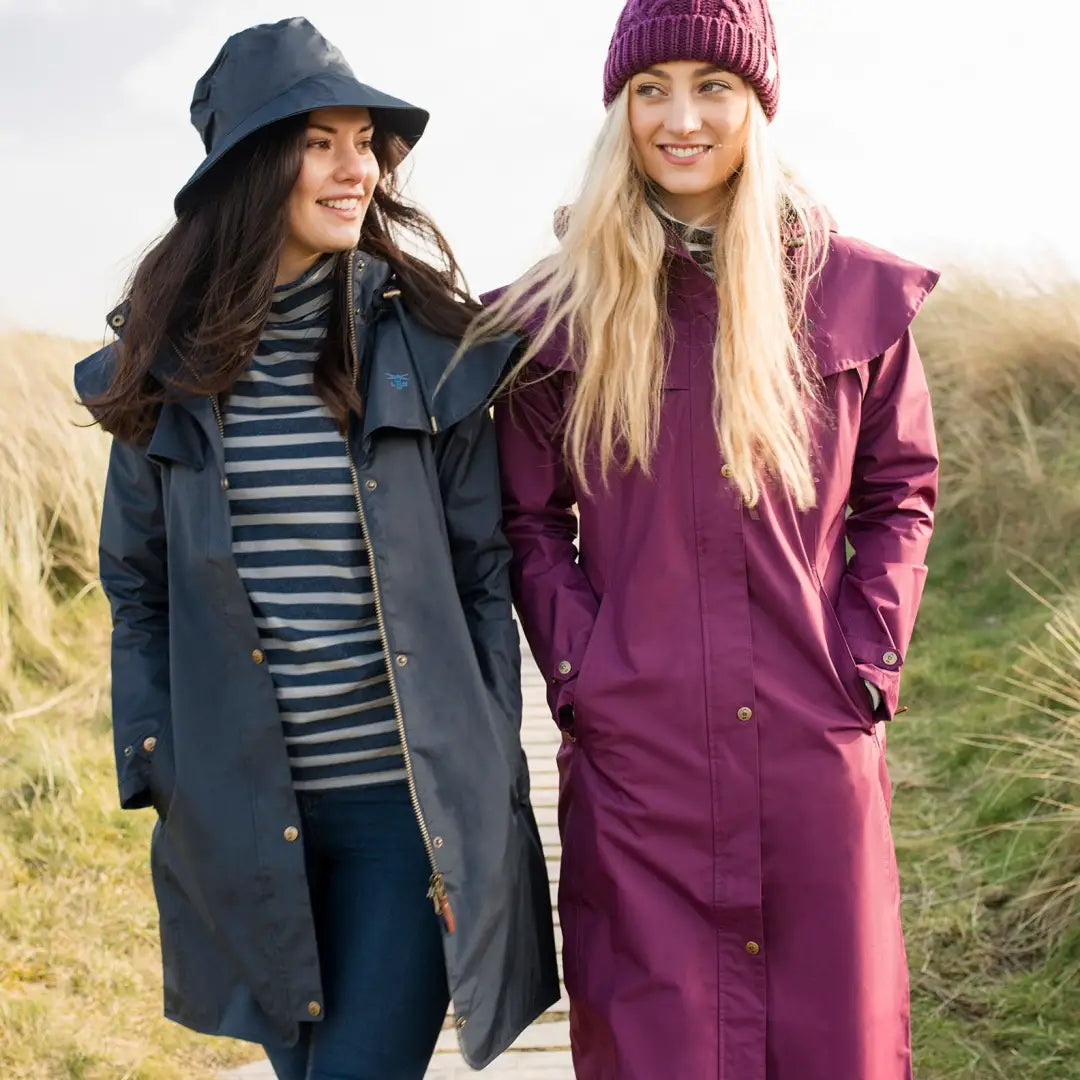 Two women in Lighthouse Outrider 3/4 length ladies waterproof raincoats and hats