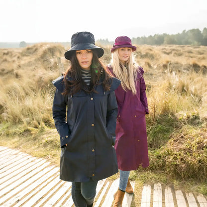 Two women in coats and hats on a walkway showcasing the Lighthouse Outrider ladies waterproof raincoat