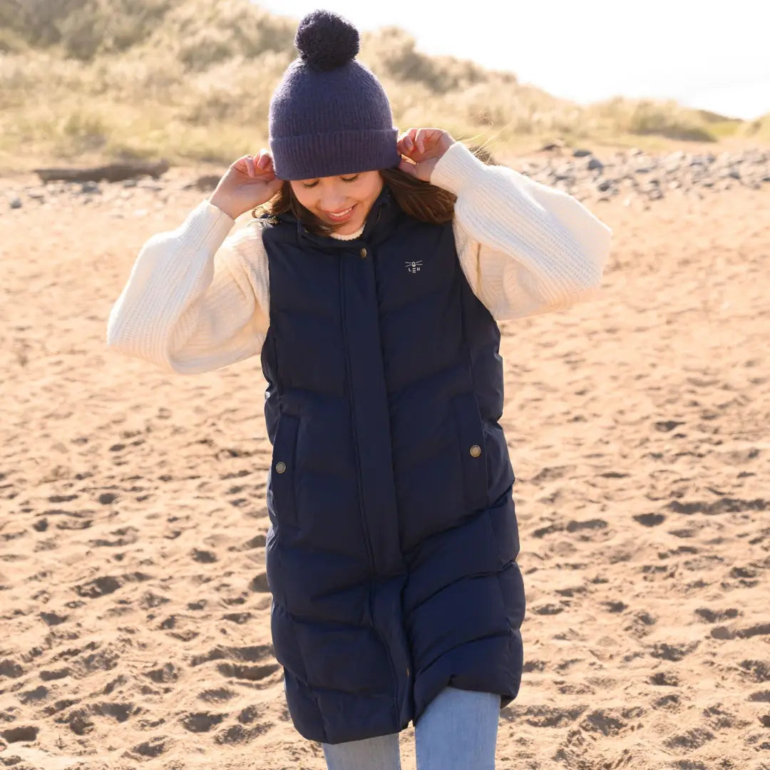 Person in navy blue puffer vest and knit hat enjoying the beach in country clothing