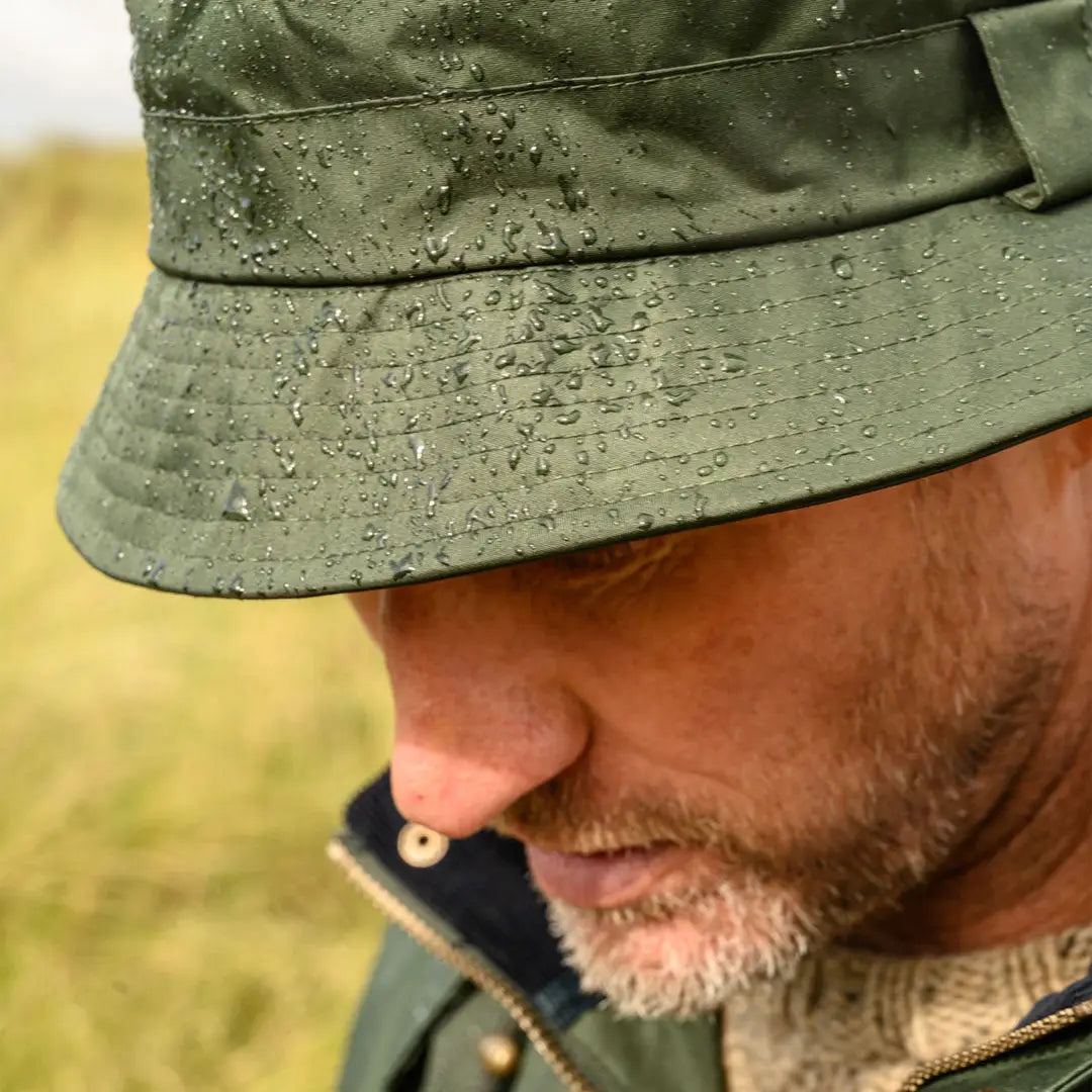 Green rain-speckled York Rain Hat on a bearded person, perfect for wet days