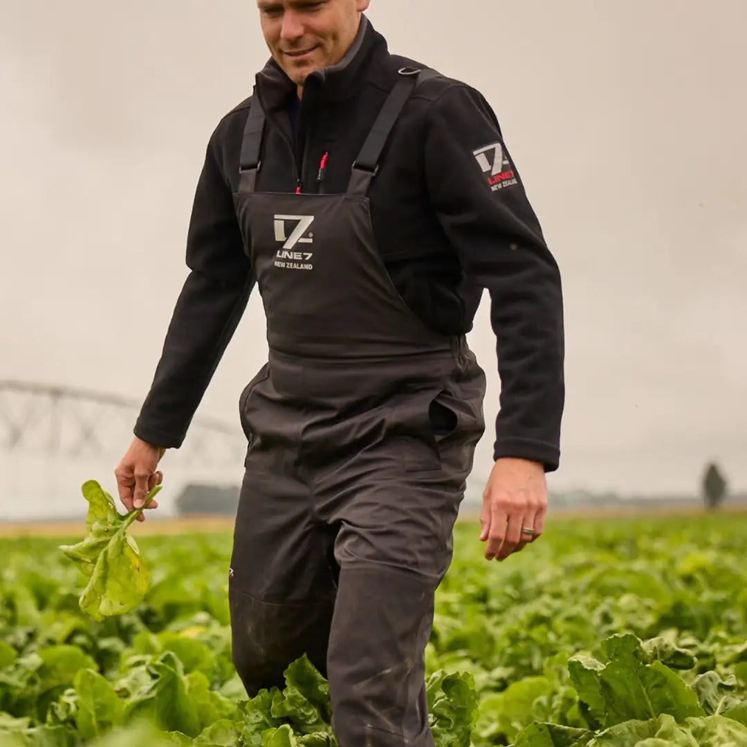 Man in dark overalls walking green crop field wearing Line 7 Storm Pro20 waterproof gear