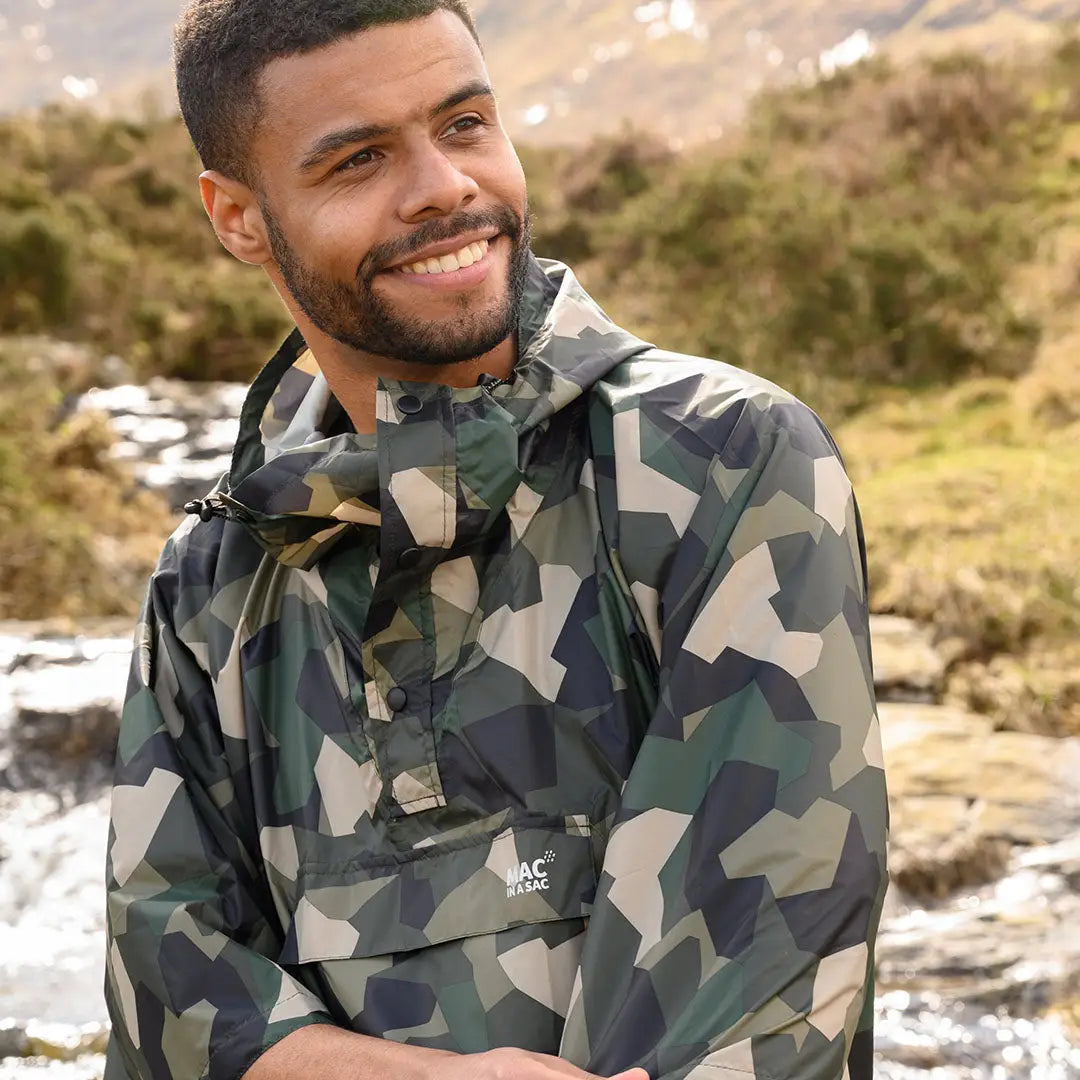 Smiling man in a Camouflage jacket wearing a Mac In A Sac Origin Poncho outdoors