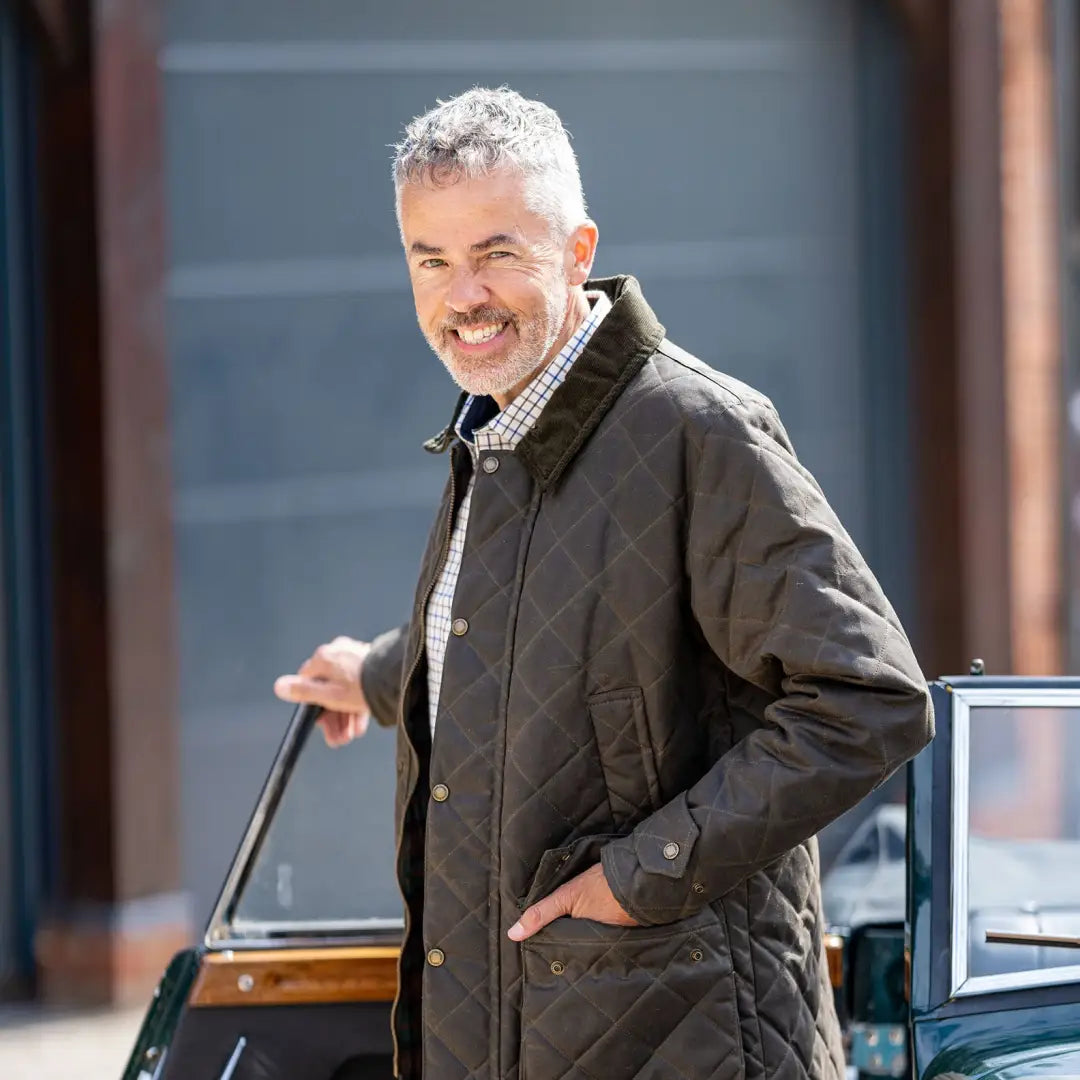 Middle-aged man in a dark quilted wax jacket smiling happily outdoors