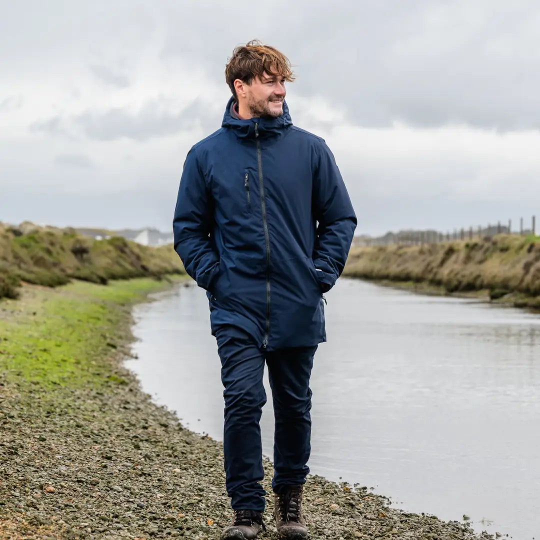 Man in a Navy Blue Musto Corsica Primaloft Rain Jacket walking by the riverbank