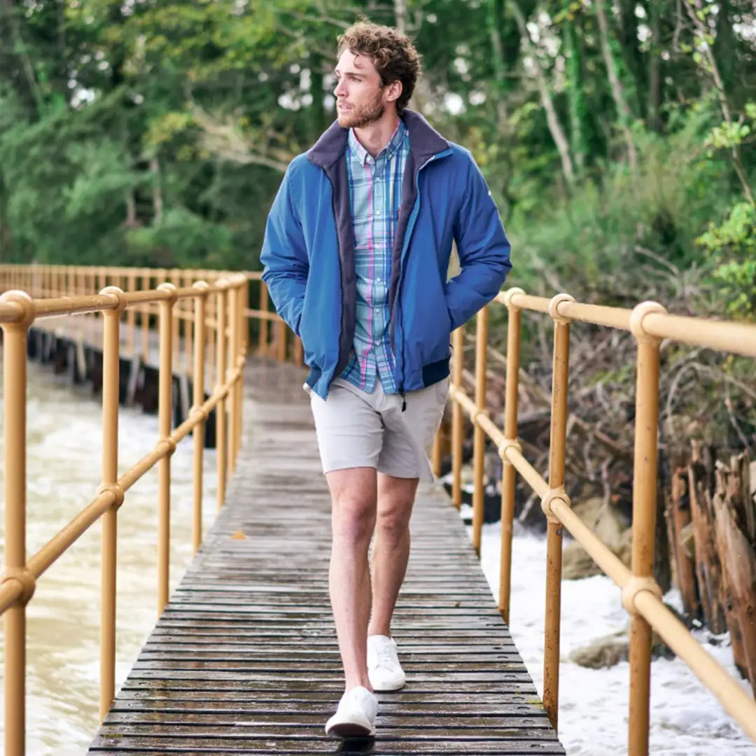 Man in blue jacket and shorts on wooden bridge, showcasing Musto Marina Plaid Long Sleeve Shirt