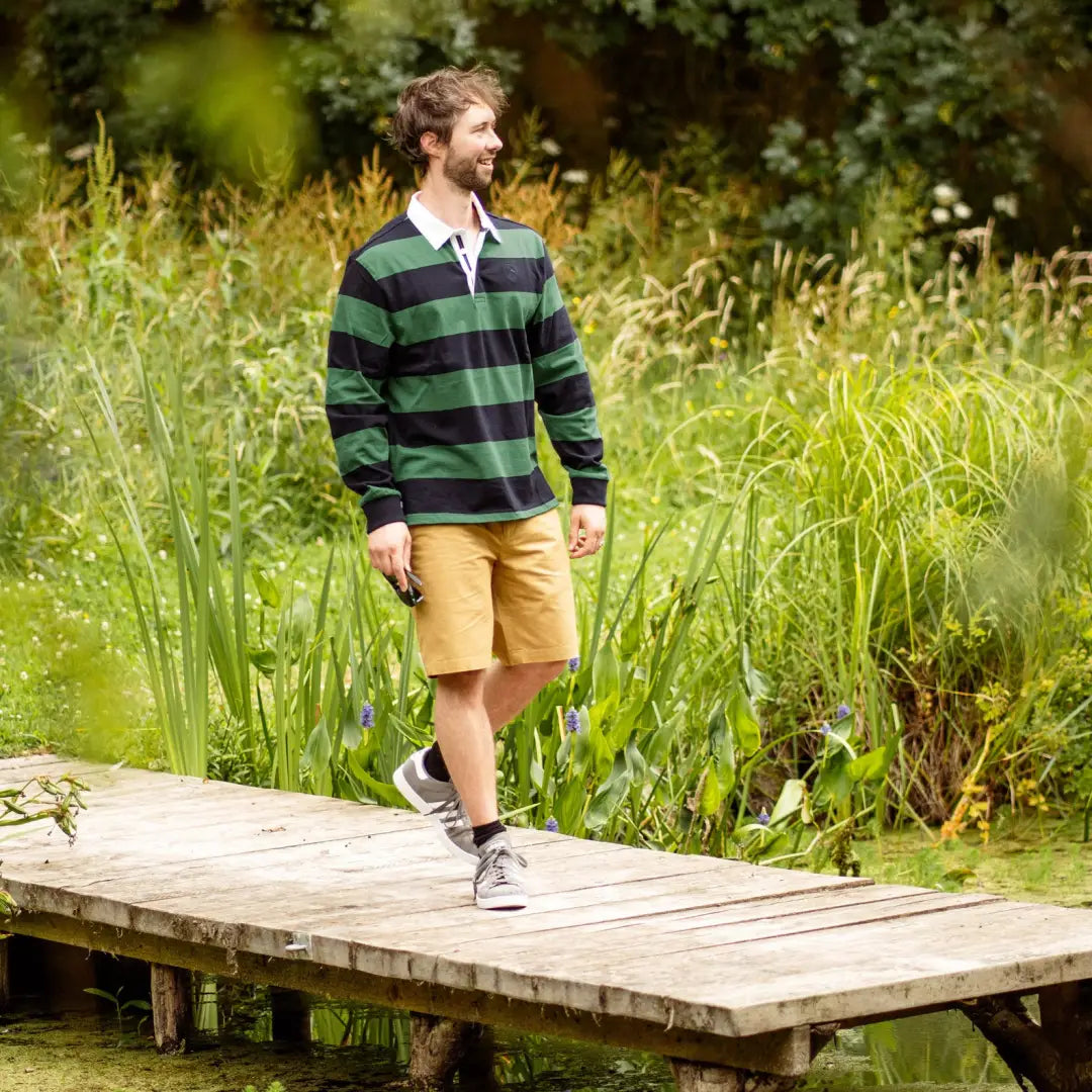 Man in a striped rugby shirt and khaki shorts strolling on a wooden dock