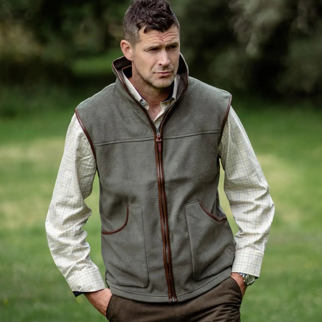 Olive green sleeveless fleece gilet with brown trim over light long-sleeved shirt