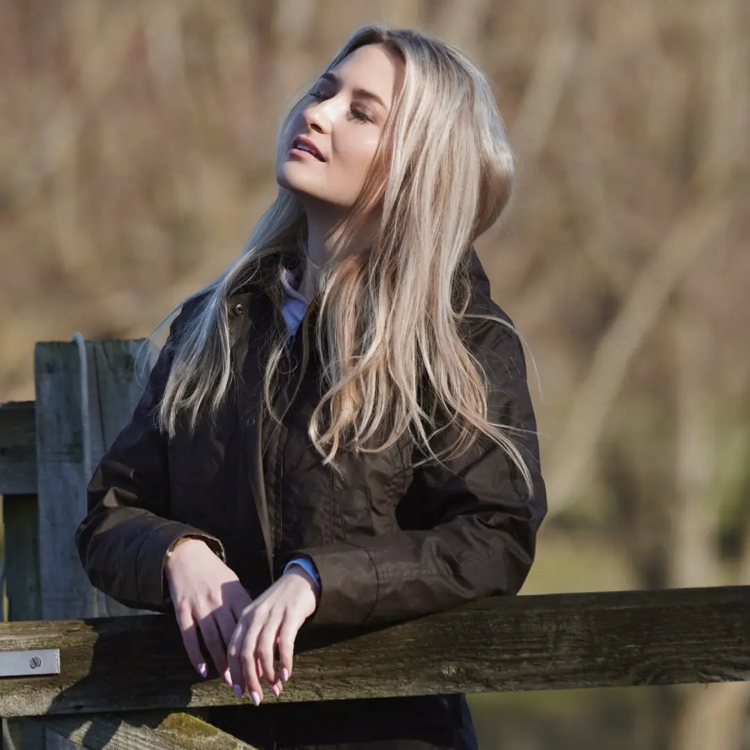 Woman with long blonde hair in a dark jacket by a fence, showcasing the Freya Ladies Wax