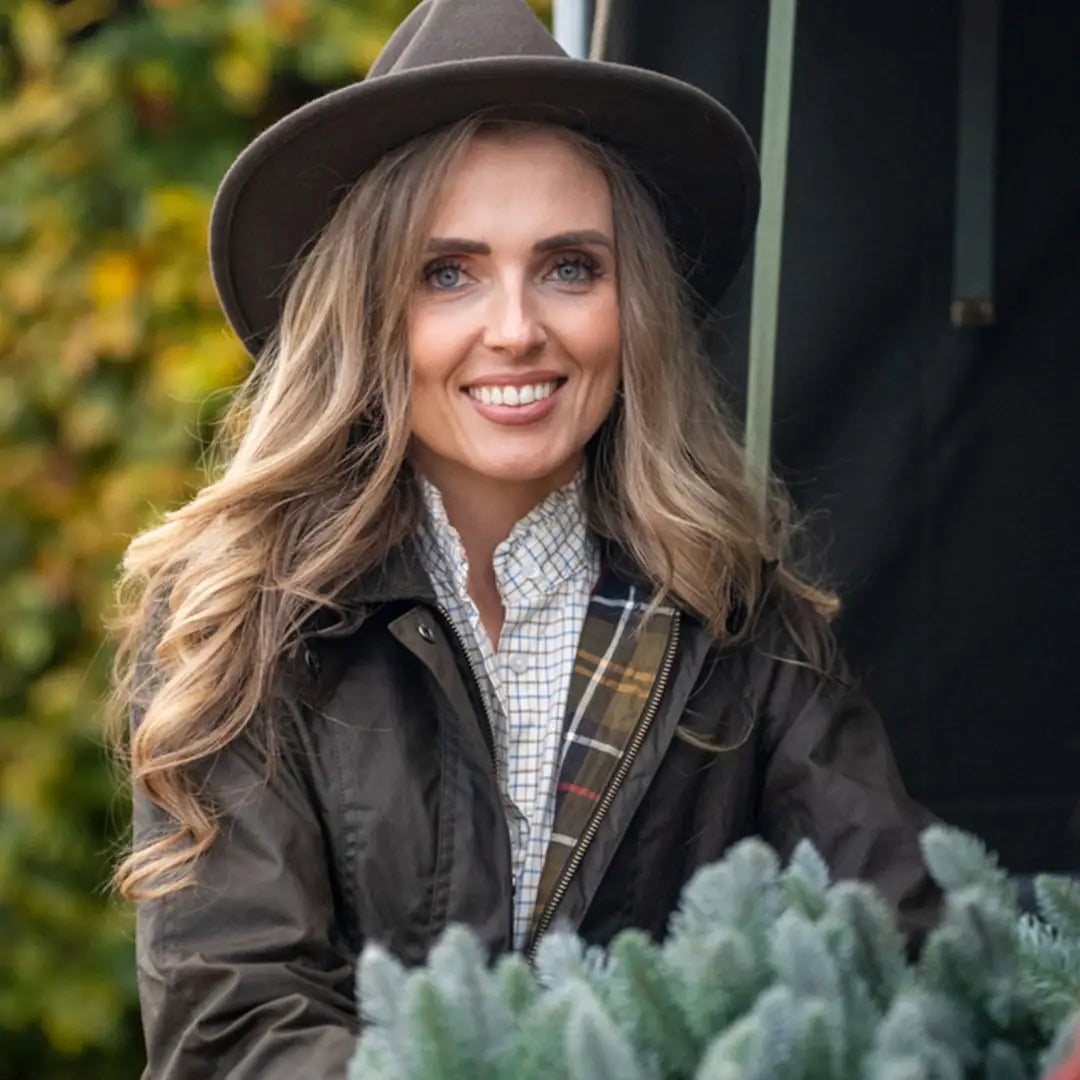 Smiling woman in a brown hat models the Forest Freya Ladies Wax Jacket