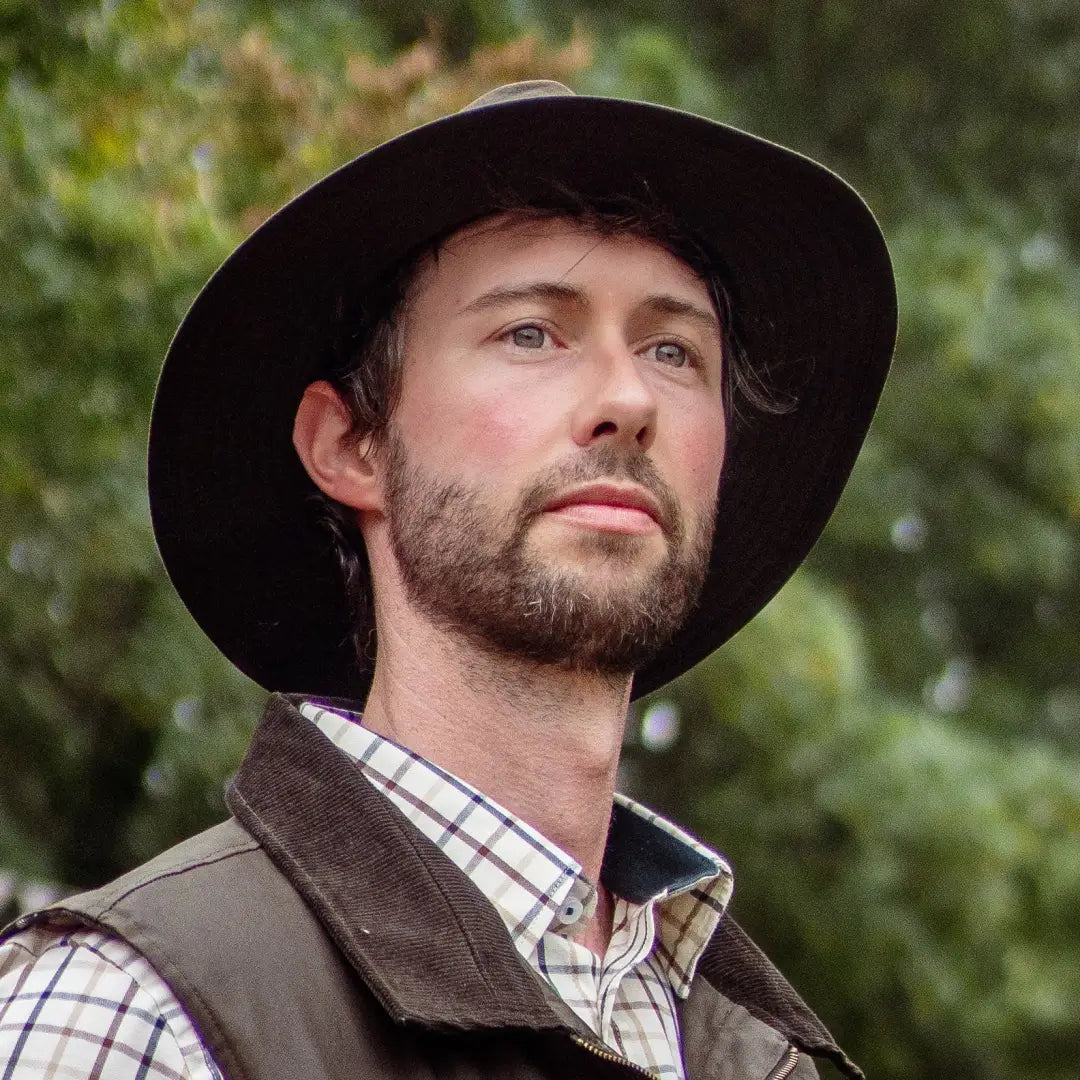 Man in a wide-brimmed hat and plaid shirt showcasing the New Forest Harrison Waxed Hat