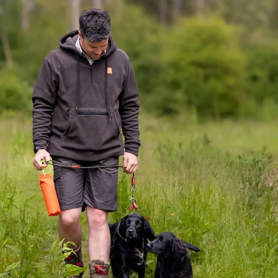 Man walking two black dogs in a grassy field wearing a Forest Heathland Hoodie