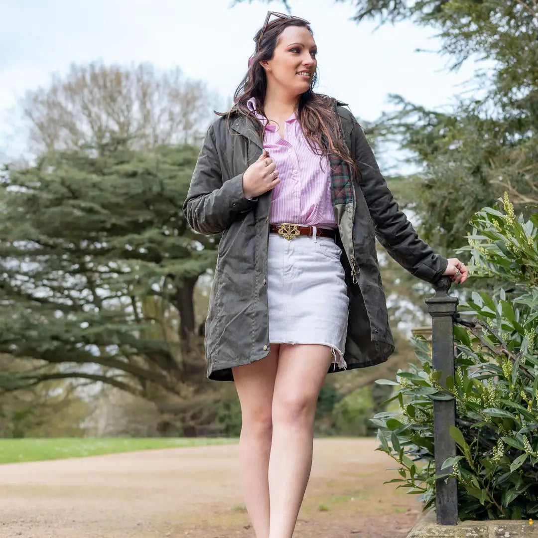 Woman in a green wax jacket, pink shirt, and white skirt enjoying country style outdoors