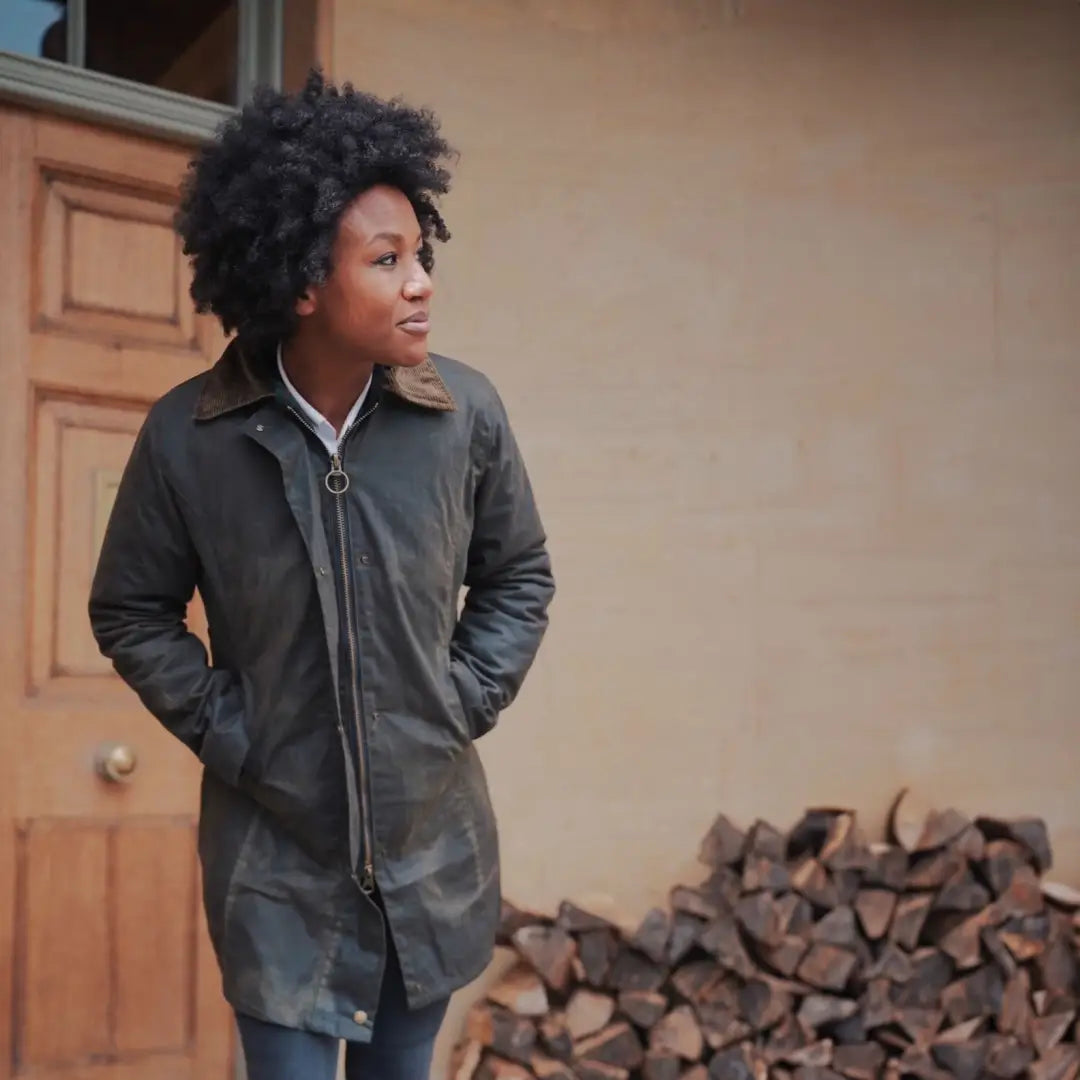 Woman with curly hair in a dark wax jacket by a wooden door, perfect for country clothing