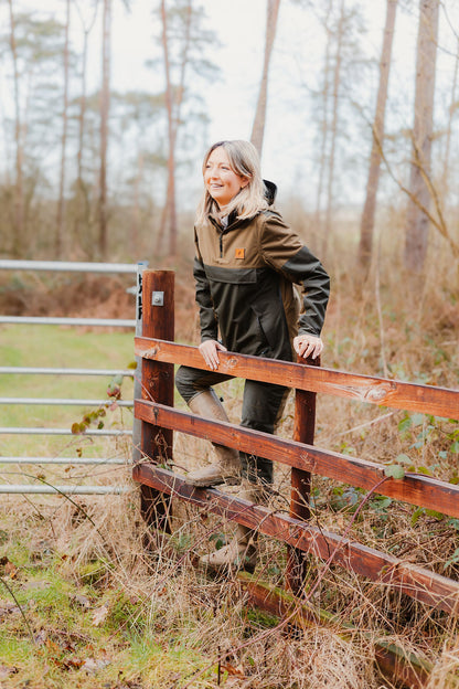 Woman in a two-tone anorak climbing a fence wearing a Forest Nightjar Smock