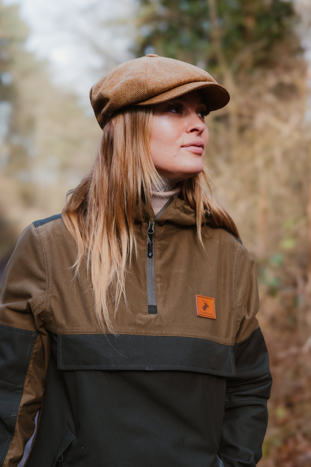 Woman in a brown tweed cap and two-tone anorak wearing a stylish Nightjar Smock