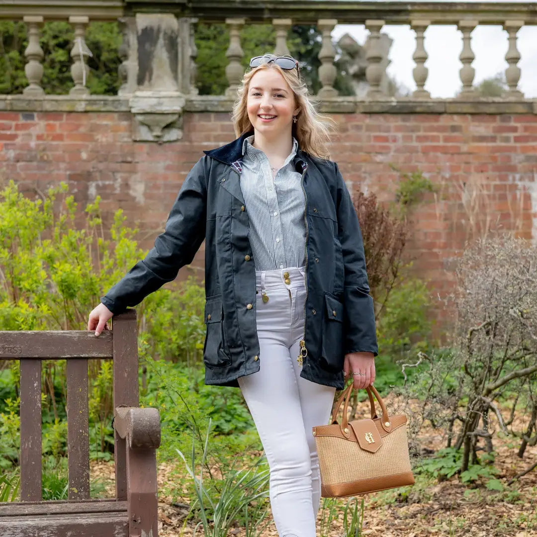 Smiling young woman in navy padded wax jacket and white pants, holding a handbag