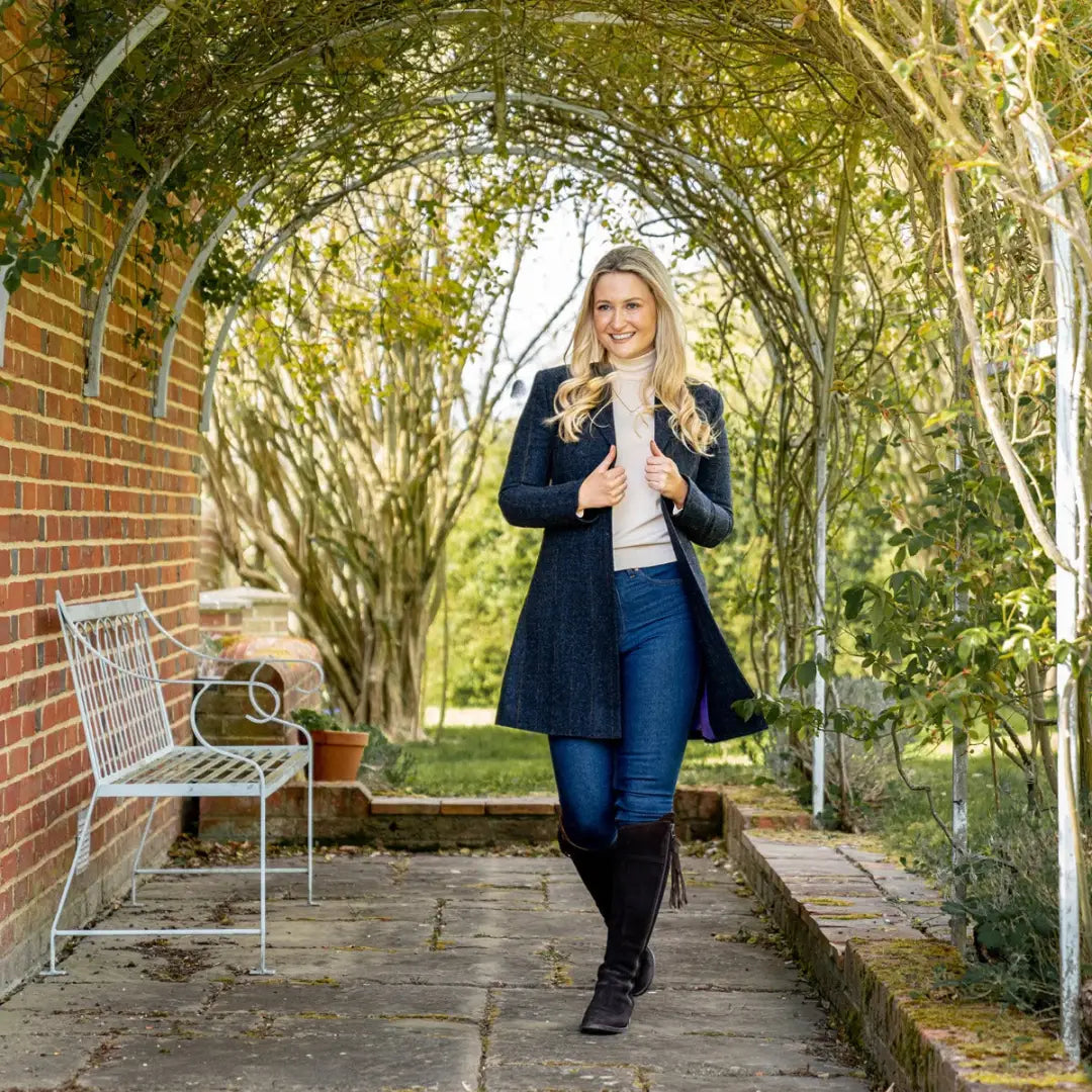 Woman strolling under a leafy archway, showcasing the stylish Forest Lizzie Tweed Coat