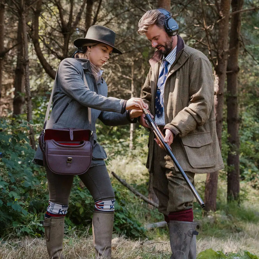 Two folks in hunting gear check out a shotgun, wearing the Maverick Waterproof Tweed Jacket